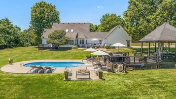 Une grande maison avec une piscine, du mobilier d’extérieur et un belvédère.
