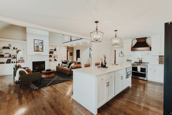 A spacious living area with a fireplace, a large island with a sink, and a kitchen with white cabinets and stainless steel appliances.