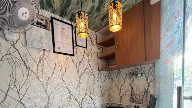 Mostrador de recepción con una botella de agua, un ventilador y una computadora. Hay dos lámparas colgantes y una pared con diseño de árbol.