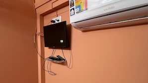Una habitación con un televisor montado, un equipo de aire acondicionado blanco y un piso cubierto de alfombra roja.
