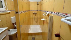 Un espacio de ducha pequeño y cerrado con bañera, inodoro y bidé.
