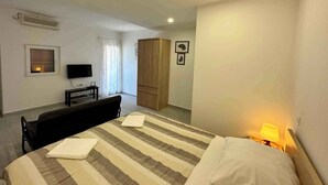 Habitación de hotel con cama, escritorio con televisor, armario y ventana con cortinas.