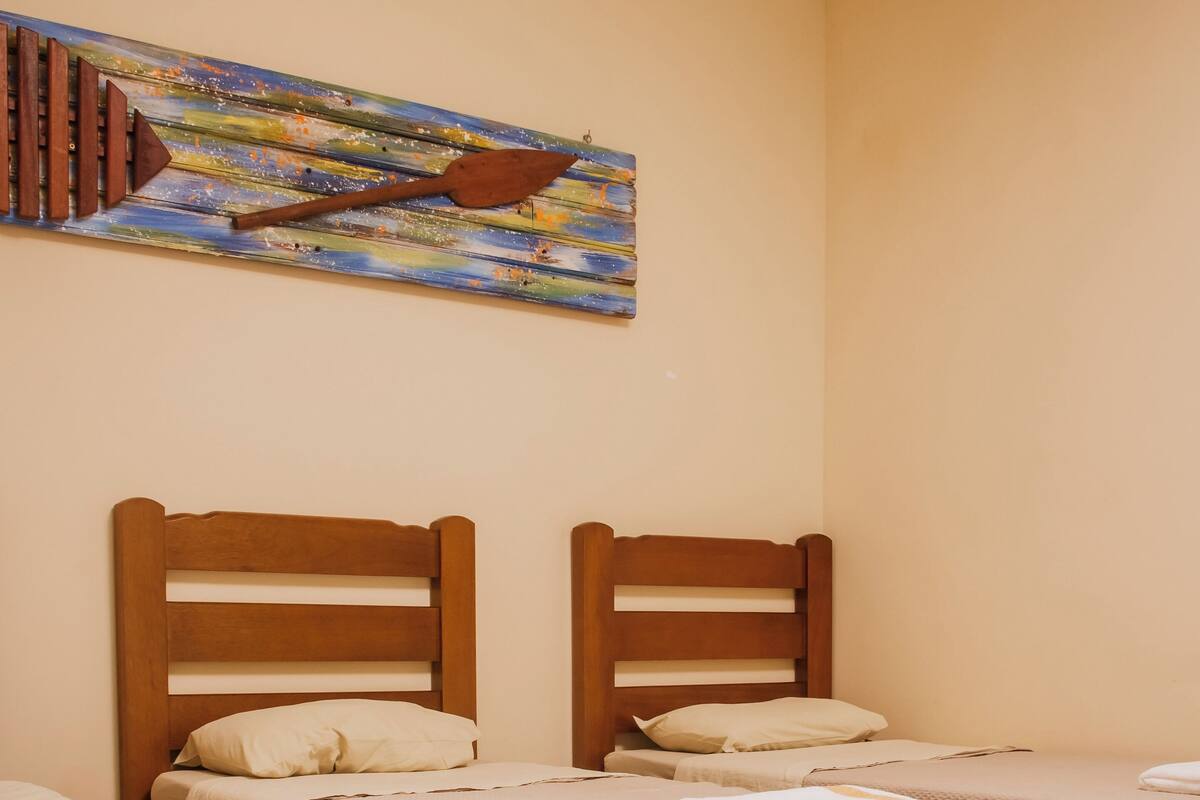 Une chambre d’hôtel avec deux lits simples, des têtes de lit en bois, une literie de couleur beige et un tableau abstrait aux couleurs vives accroché au mur.