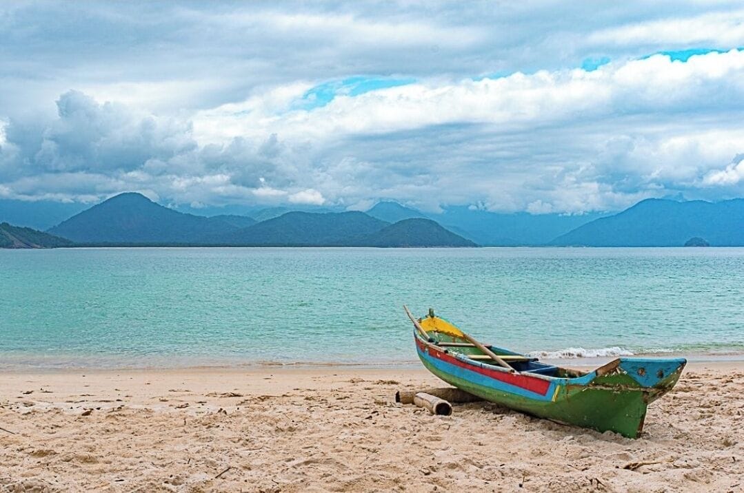 A beach with a colorful boat on the sand and mountains in the background.