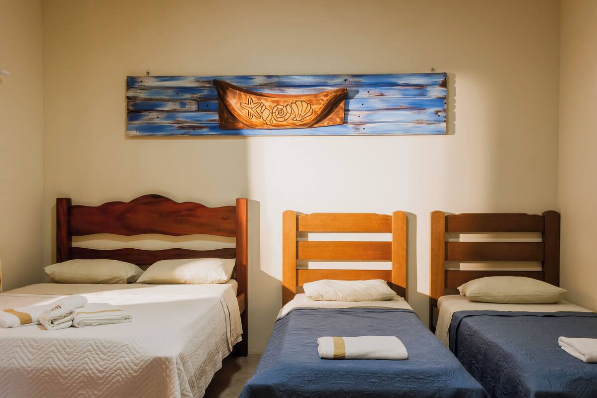 Une chambre d’hôtel avec deux lits simples, chacun doté d’une tête de lit en bois, de draps blancs et d’une serviette sur le lit. Un tableau représentant un bateau est accroché au mur, au-dessus des lits.