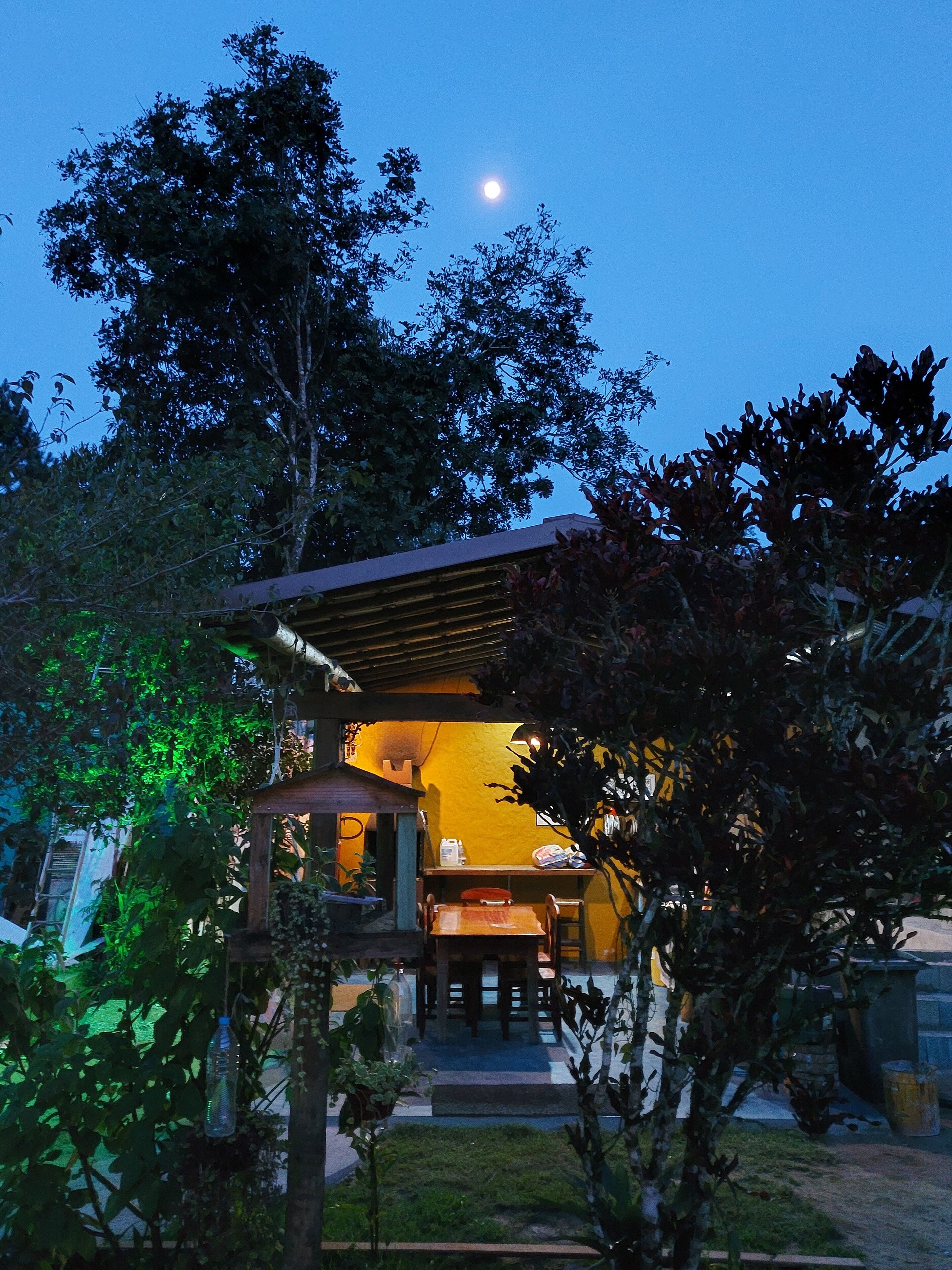 Una casa con terraza de madera, un comedor con mesa y sillas, y un pequeño jardín.
