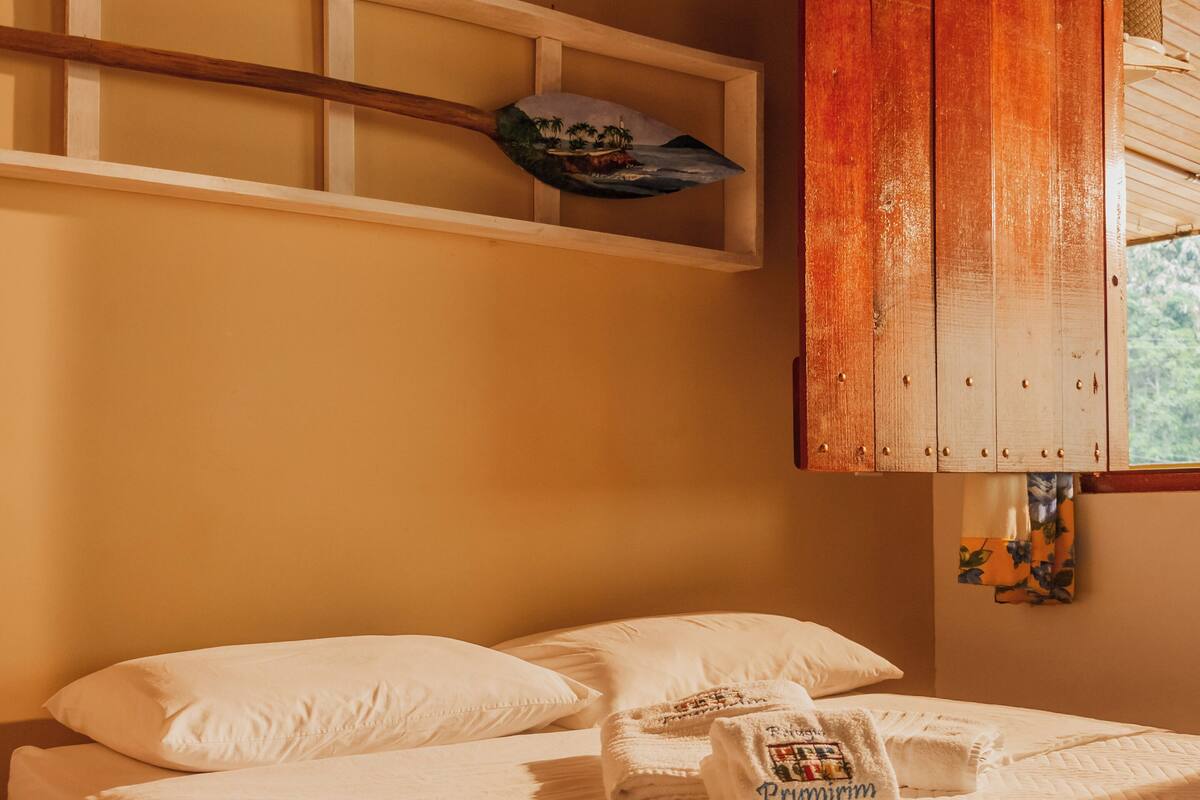 Un lit bien fait, avec du linge de lit blanc, une tête de lit en bois et une petite étagère au-dessus.