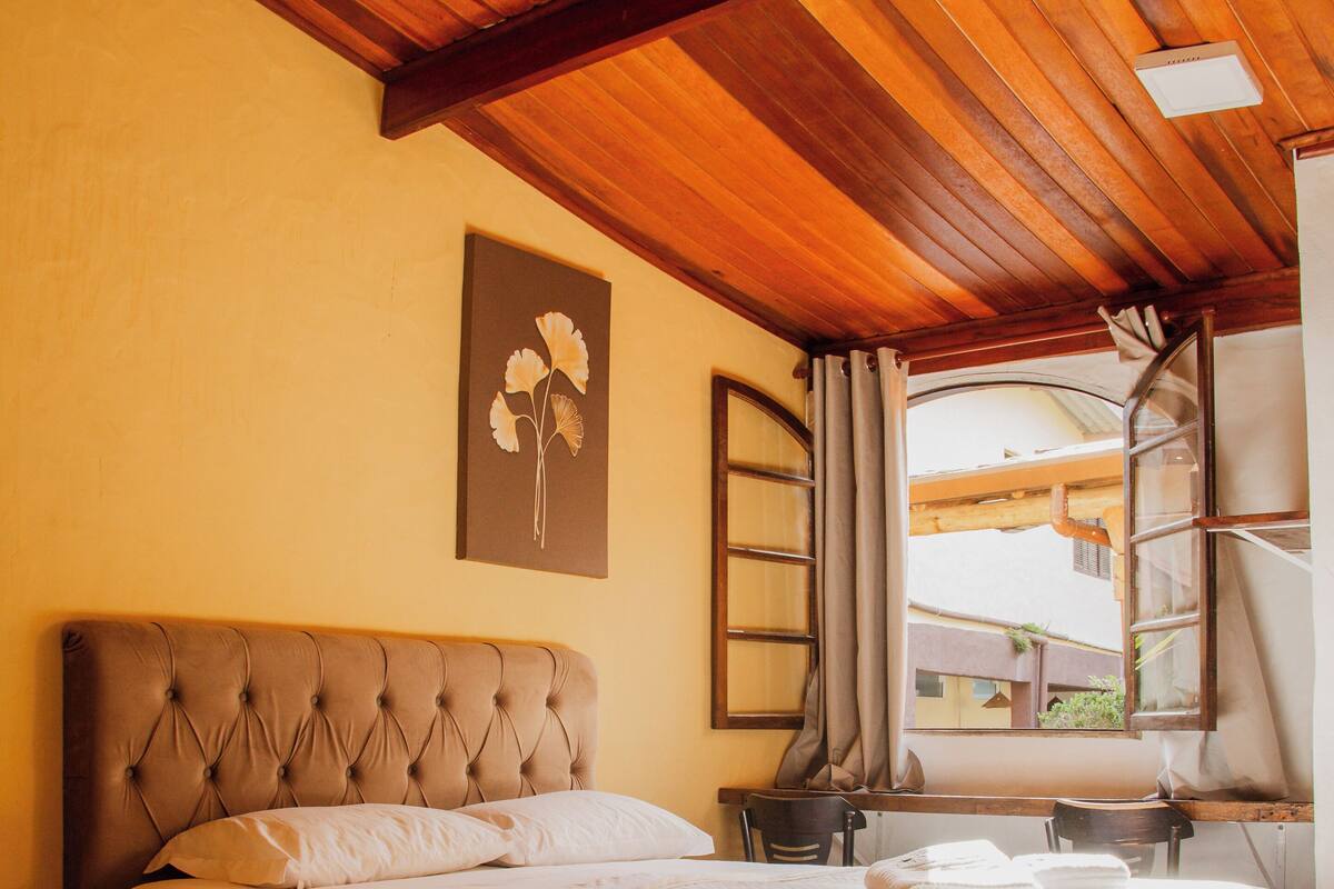 Une chambre à coucher avec un grand lit, une tête de lit, une fenêtre avec des rideaux et un plafond en bois.