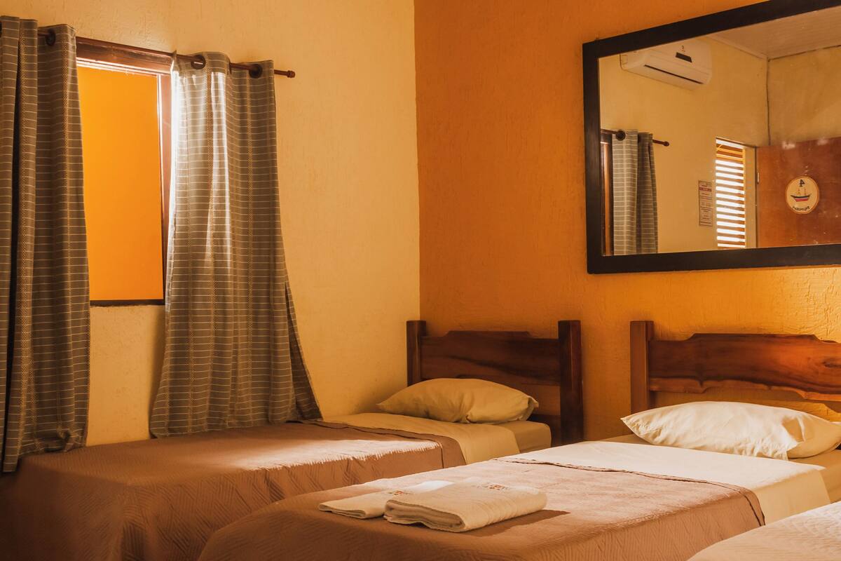 Une chambre d’hôtel avec deux lits simples, une tête de lit en bois, un grand miroir et une fenêtre avec des rideaux.