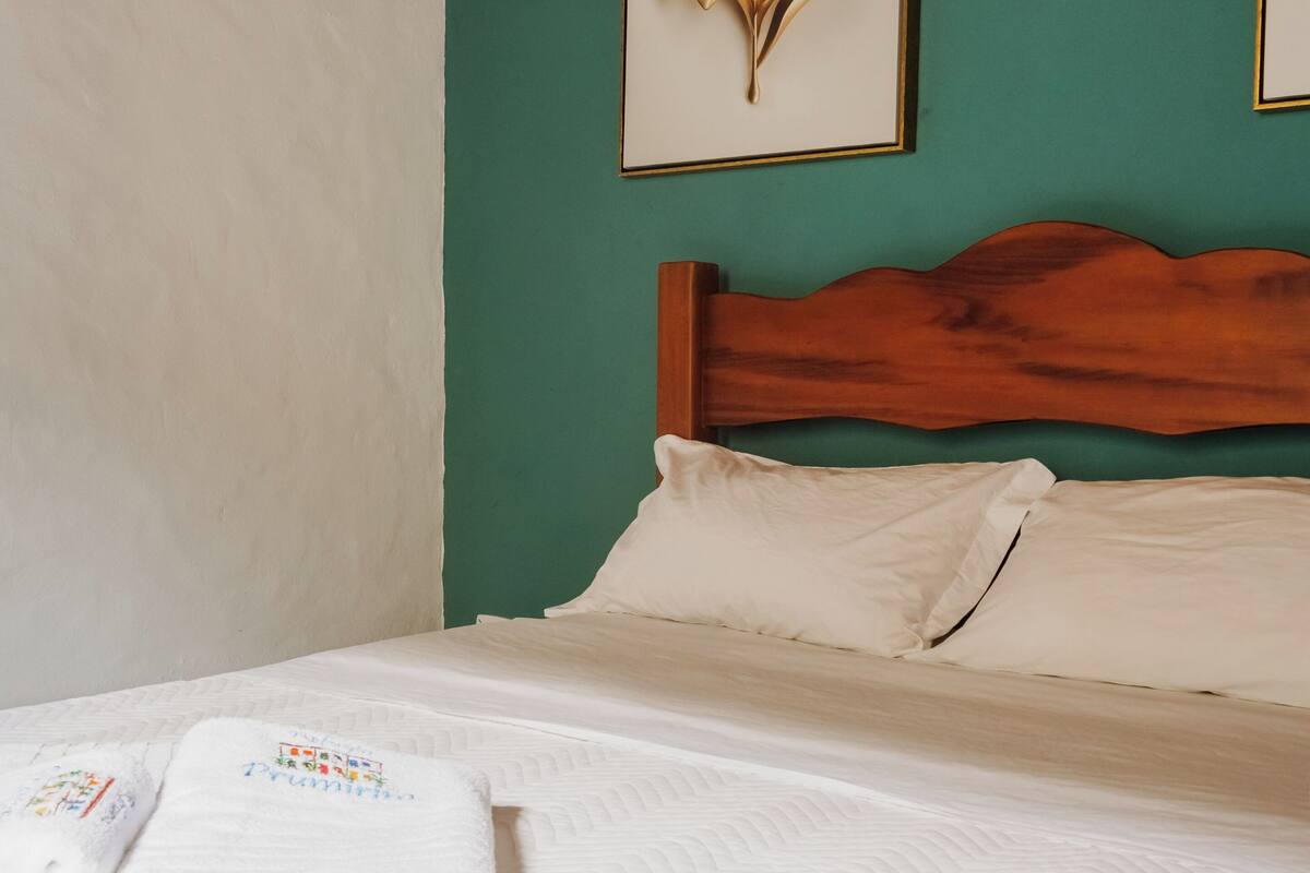 Un lit bien fait, avec du linge de lit blanc et des oreillers, une tête de lit en bois et un mur de couleur turquoise.