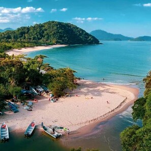 A beach with boats, a sandy shore, and a forested hill in the background. - Pousada Refugio Prumirim (Ubatuba)