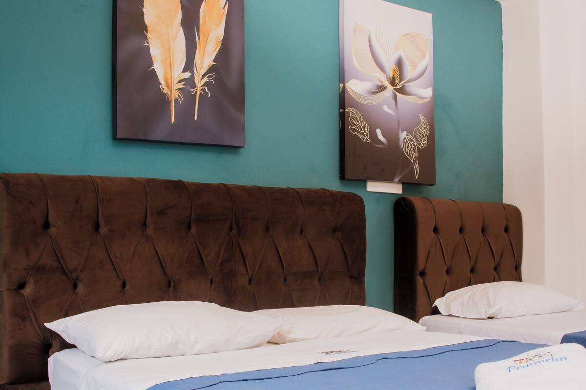Une chambre à coucher avec un grand lit, une tête de lit capitonnée et deux tableaux accrochés au mur.