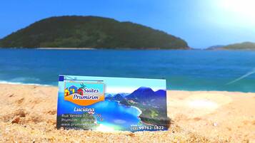 A brochure for 'Suites Prumirim' with a beach view, contact number, and website.