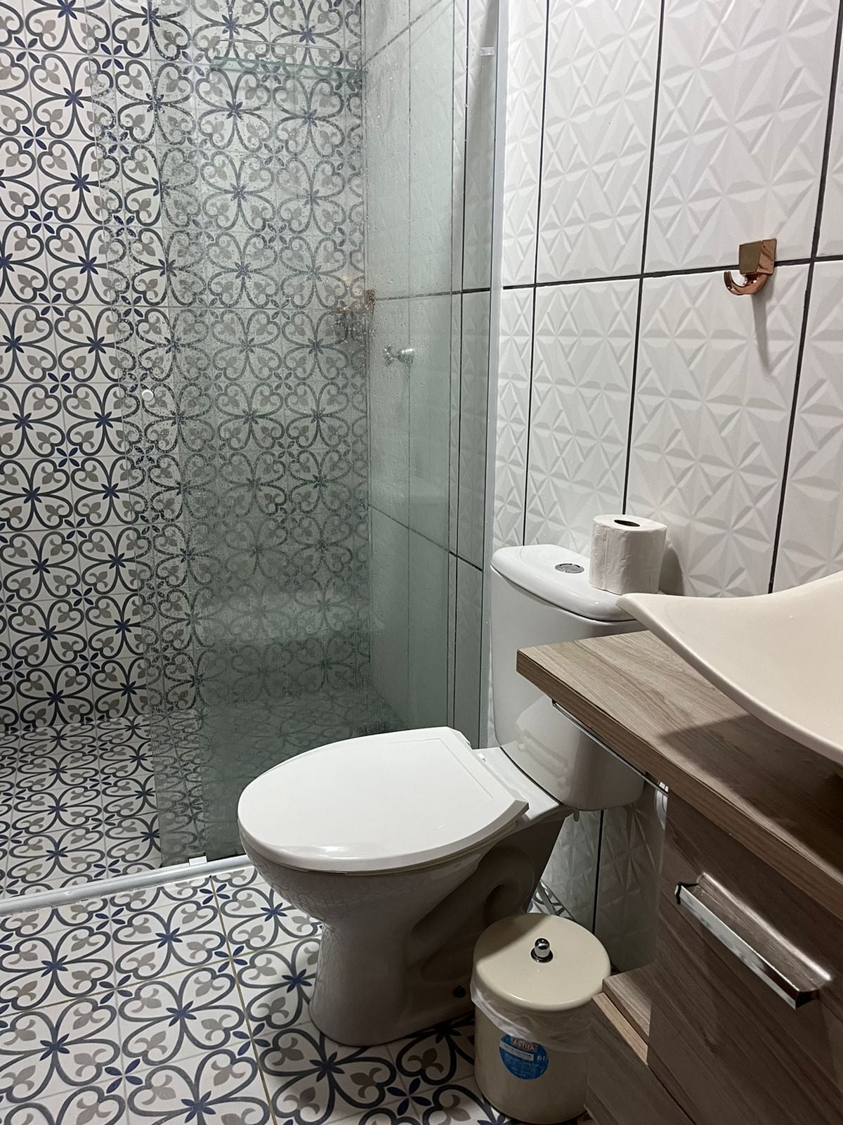 Um banheiro com piso estampado, vaso sanitário, box de chuveiro e um espelho sobre uma toucador de madeira.