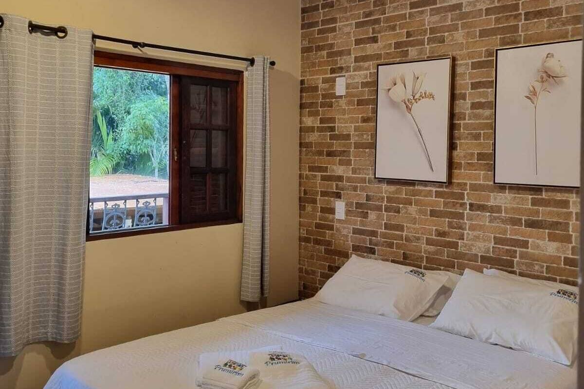 Une chambre avec un plafond en bois, un mur en briques, un lit recouvert de draps blancs et deux tableaux encadrés accrochés au mur.