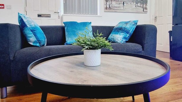 A living room with a dark blue sofa, a round coffee table with a plant, and a painting of a cityscape on the wall.