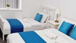 A hotel room with two beds, a nightstand, a lamp, and a window with blinds.