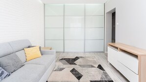 Ein modernes Wohnzimmer mit einem grauen Sofa, einem Holz-TV-Schrank und einem gemusterten Teppich.