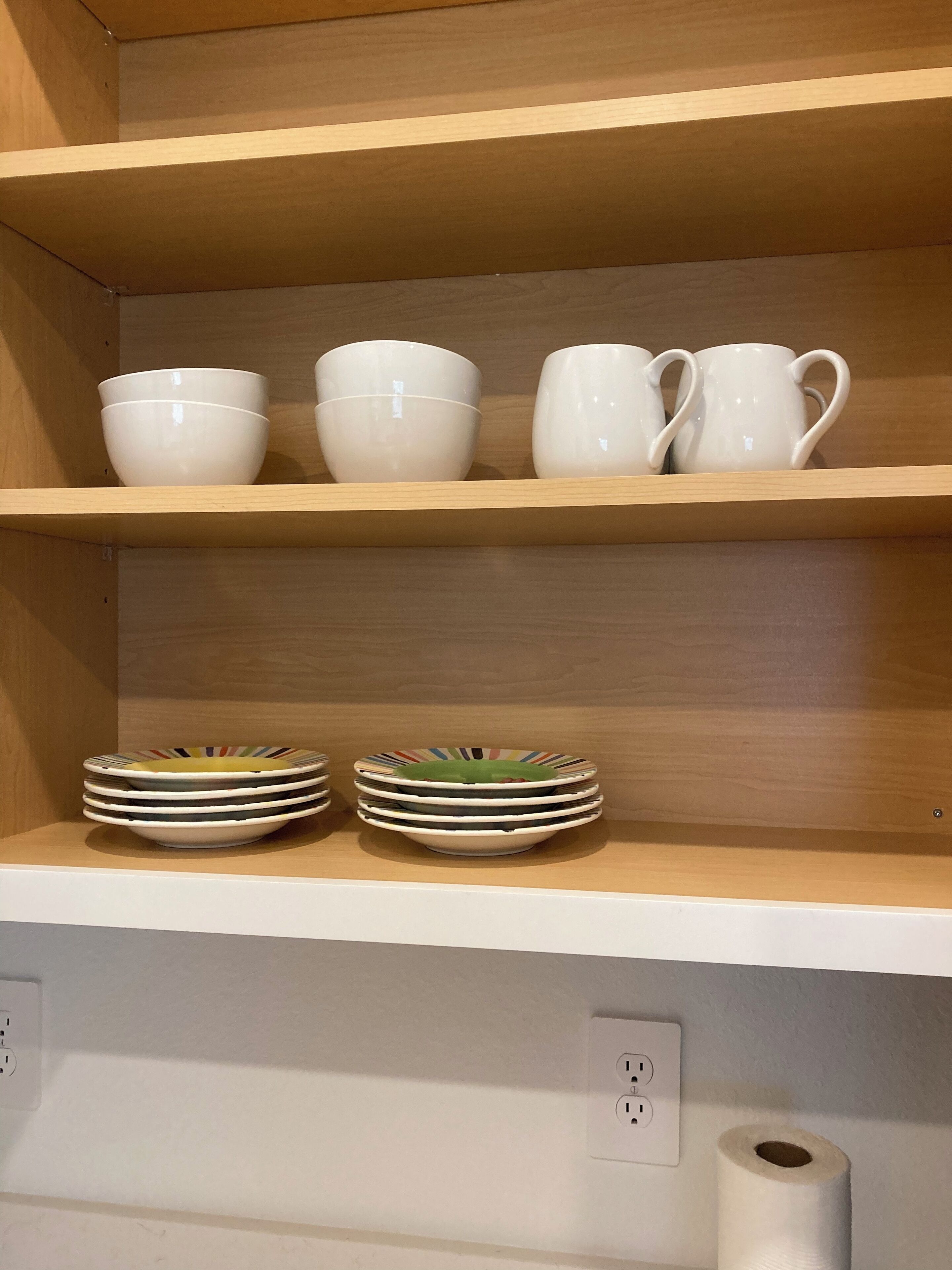 En hylla med vita skålar och tallrikar.