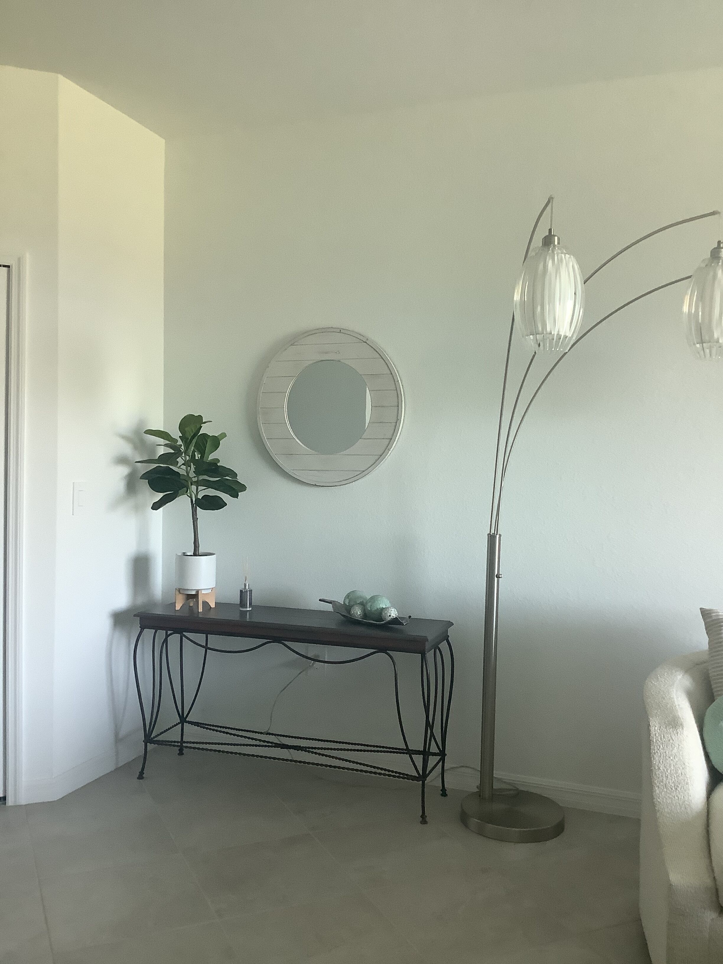 A room with a round mirror on the wall, a small table with a potted plant, and a floor lamp.