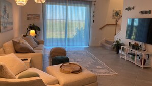 Een woonkamer met een bank, een poef en een televisie op een standaard.