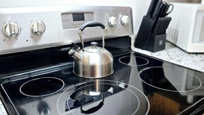 Une cuisine avec une bouilloire en acier inoxydable posée sur une plaque de cuisson noire, un four à micro-ondes et un bloc à couteaux.