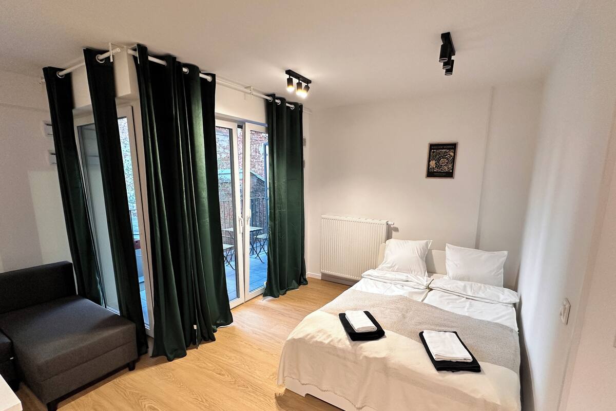 A bedroom with a bed, a chair, a radiator, and a view of the outside.