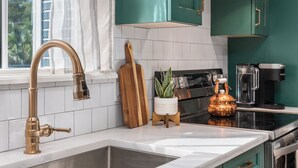 Een keuken met smaragdgroene kastjes, een roestvrijstalen spoelbak, een koperen waterkoker en een houten snijplank.