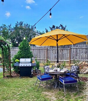 En baghave med grill, udendørs bord og stole samt en gul parasol.
