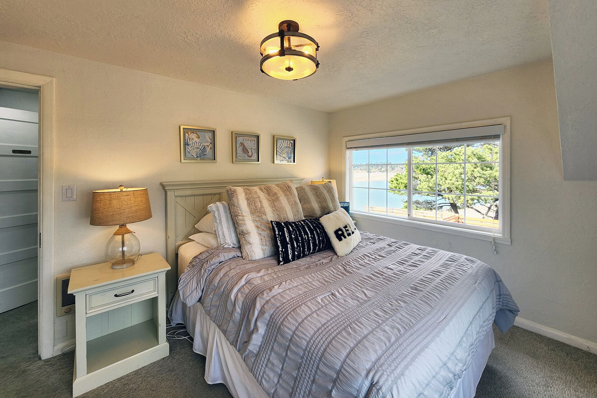 A bedroom with a bed, a nightstand, a lamp, a window with a view, and wall art.