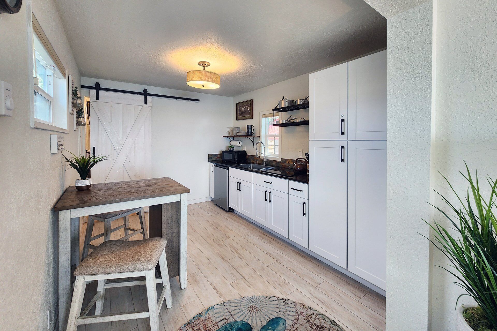 Una cocina compacta con armarios blancos, una mesa de madera y una lámpara colgante.