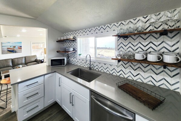 Una cocina moderna con armarios blancos, un lavamanos de acero inoxidable y una ventana con vista a la playa.