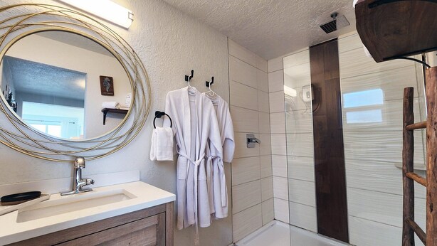 Une salle de bain moderne avec un grand miroir, un meuble-lavabo en bois, des serviettes blanches et un espace douche.