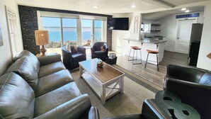 Un salon moderne avec un canapé en cuir, une table basse et un téléviseur. Il y a également un coin cuisine avec un bar et une enseigne sur laquelle on peut lire « PLAGE ».