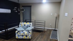 Una habitación con un sillón estampado, un banco de metal negro, una lámpara de pie y un tapete con diseño.