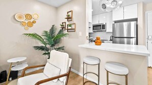 A modern kitchen with white cabinets, a stainless steel refrigerator, and a bar area with stools. - Peaceful Modern HNL Getaway (Honolulu)