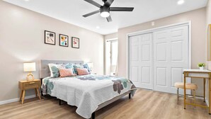 A bedroom with a bed, bedside table, lamp, ceiling fan, and a door. - Peaceful Modern HNL Getaway (Honolulu)