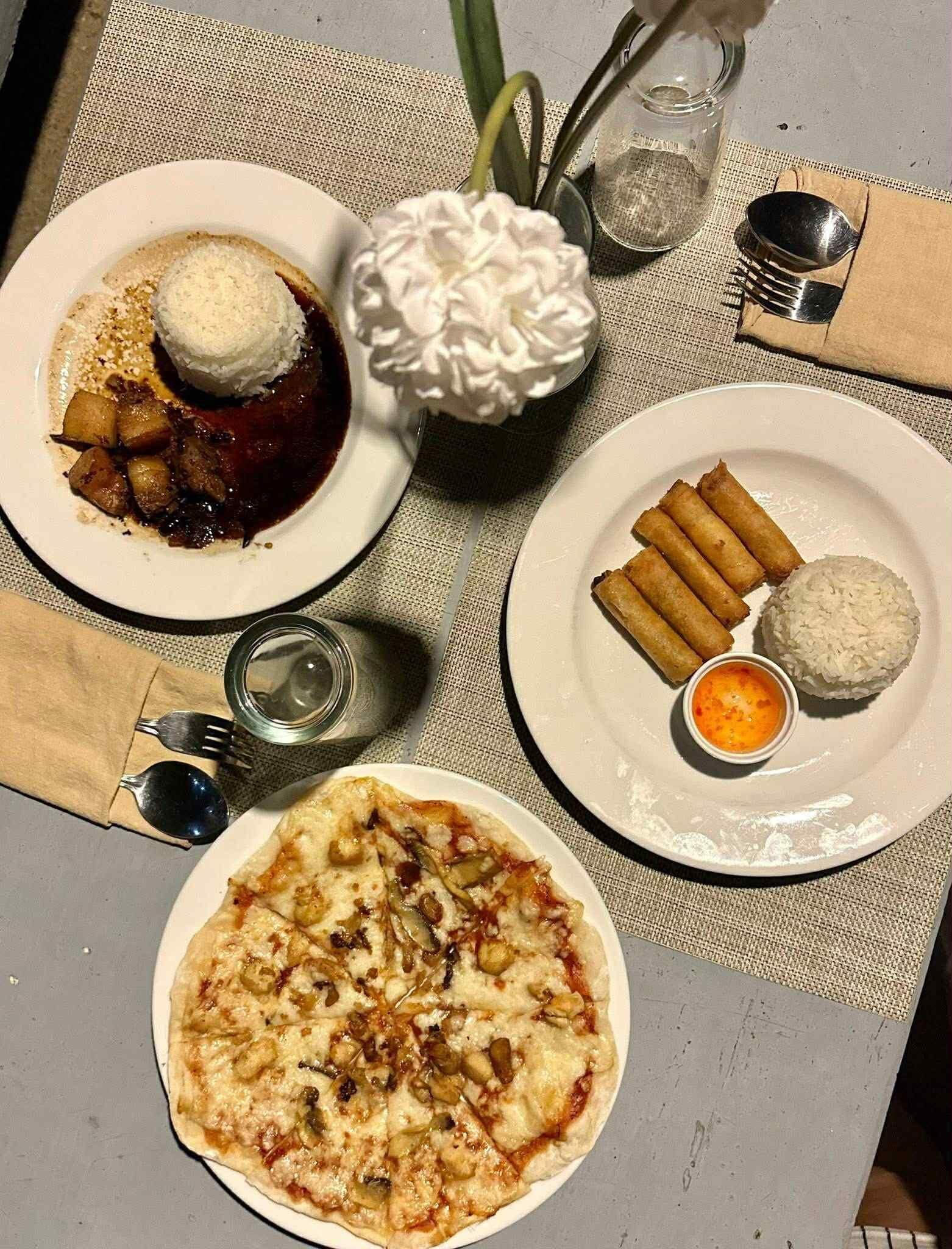 Una mesa con platos de comida que incluyen pizza, arroz con acompañamientos fritos y un postre con crema batida.