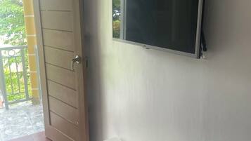 A room with a door, a wall-mounted TV, a small table with a decorative mat, and a remote control on the table.