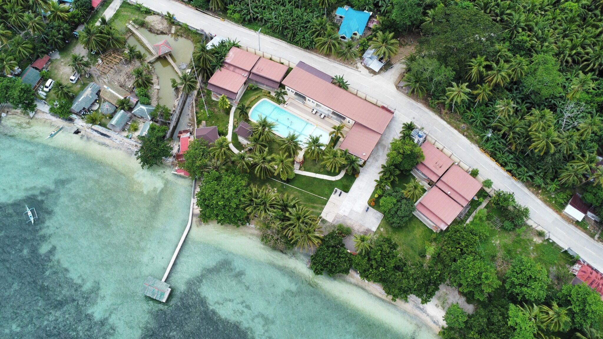 Vista aérea de una propiedad costera con piscina, muelle y exuberante vegetación.