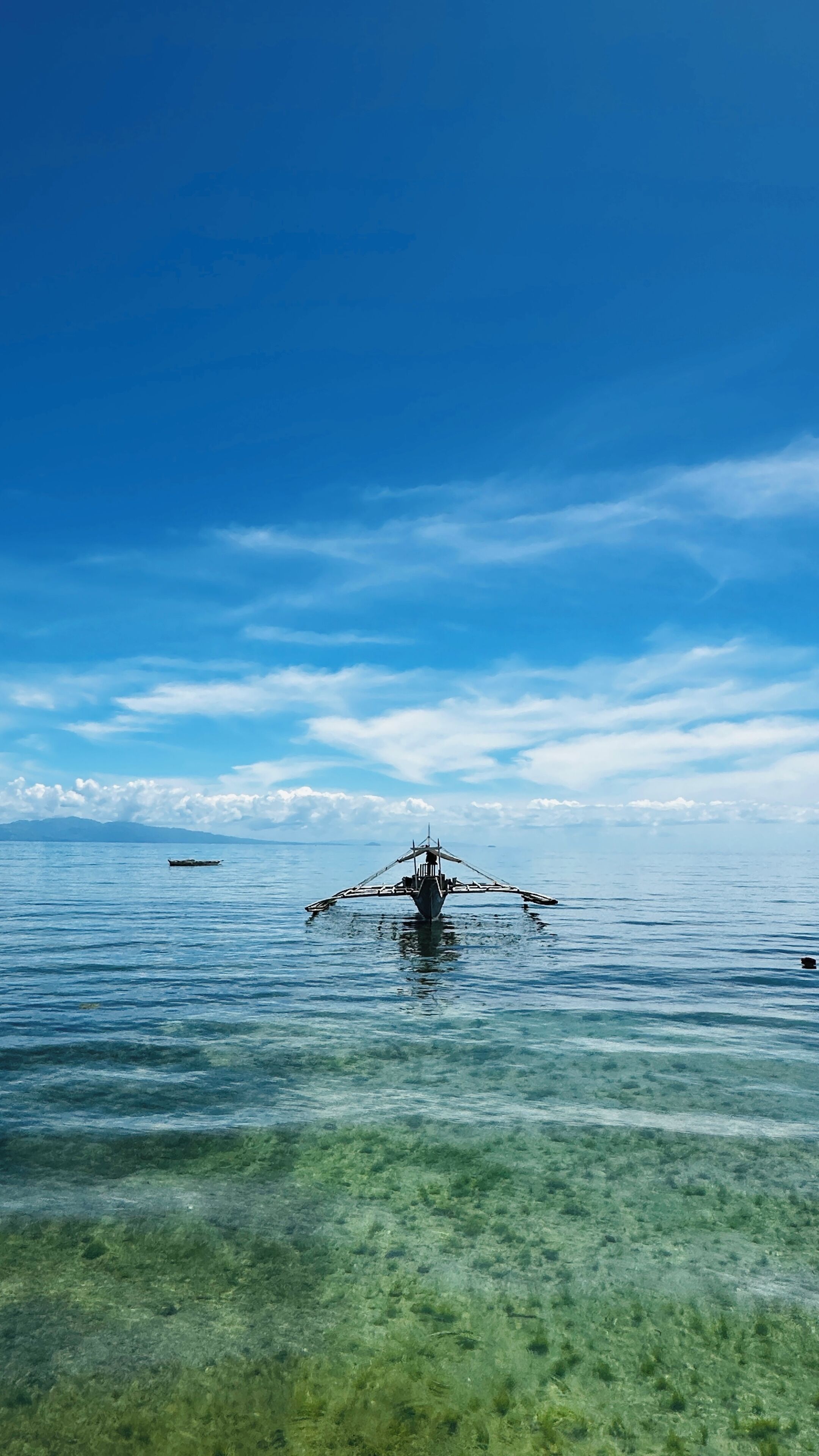A clear view of a boat in calm waters with a distant mountain range and a clear sky.