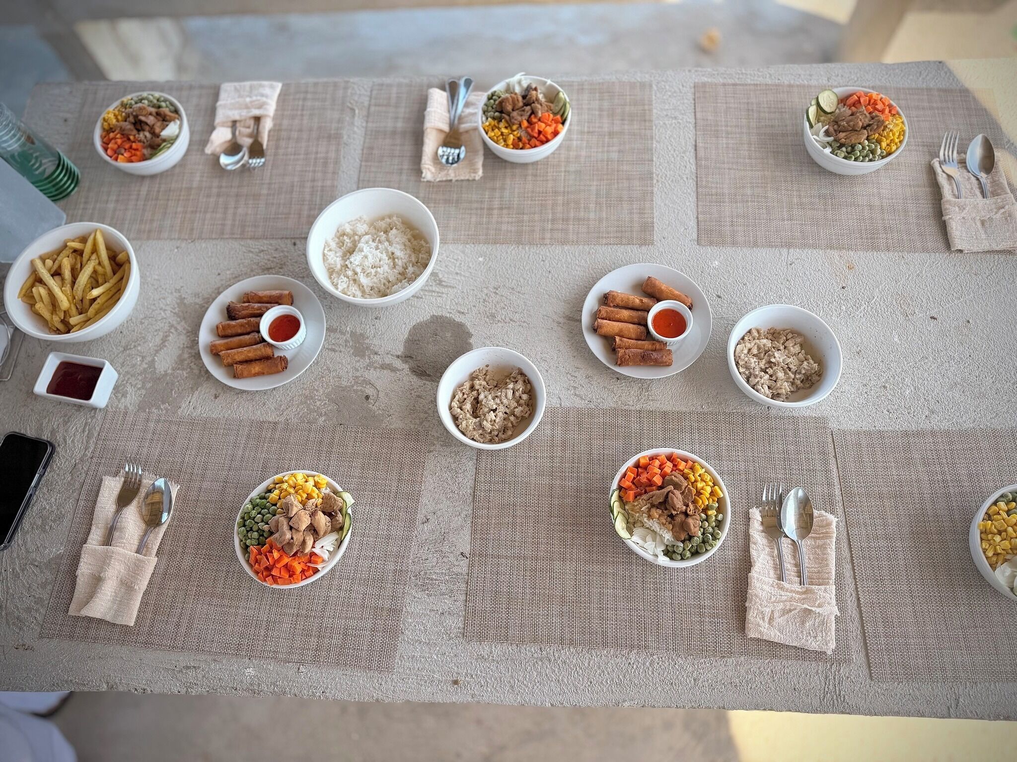 Une table dressée avec divers plats, notamment du riz, des légumes et des aliments frits, disposés sur une nappe à motifs.