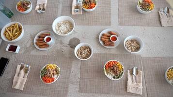 A table set with various dishes including rice, vegetables, and fried items, arranged on a textured tablecloth.