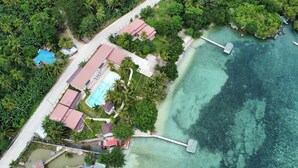 An aerial view of a coastal property with a swimming pool, a dock, and lush greenery.