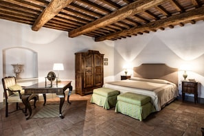 A bedroom with a wooden ceiling, a bed with a headboard, two bedside tables with lamps, a wooden cabinet, a chair, and a small table with a globe.