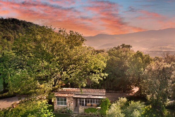 A stone house with a tiled roof surrounded by lush greenery and trees.