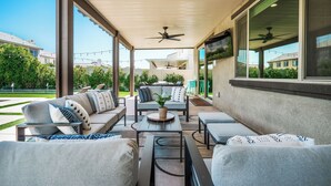 An outdoor patio area with a sofa set, a table, and ceiling fans. - Paseo Palms, Modern 6br home 5min to Polo Grounds (Coachella)