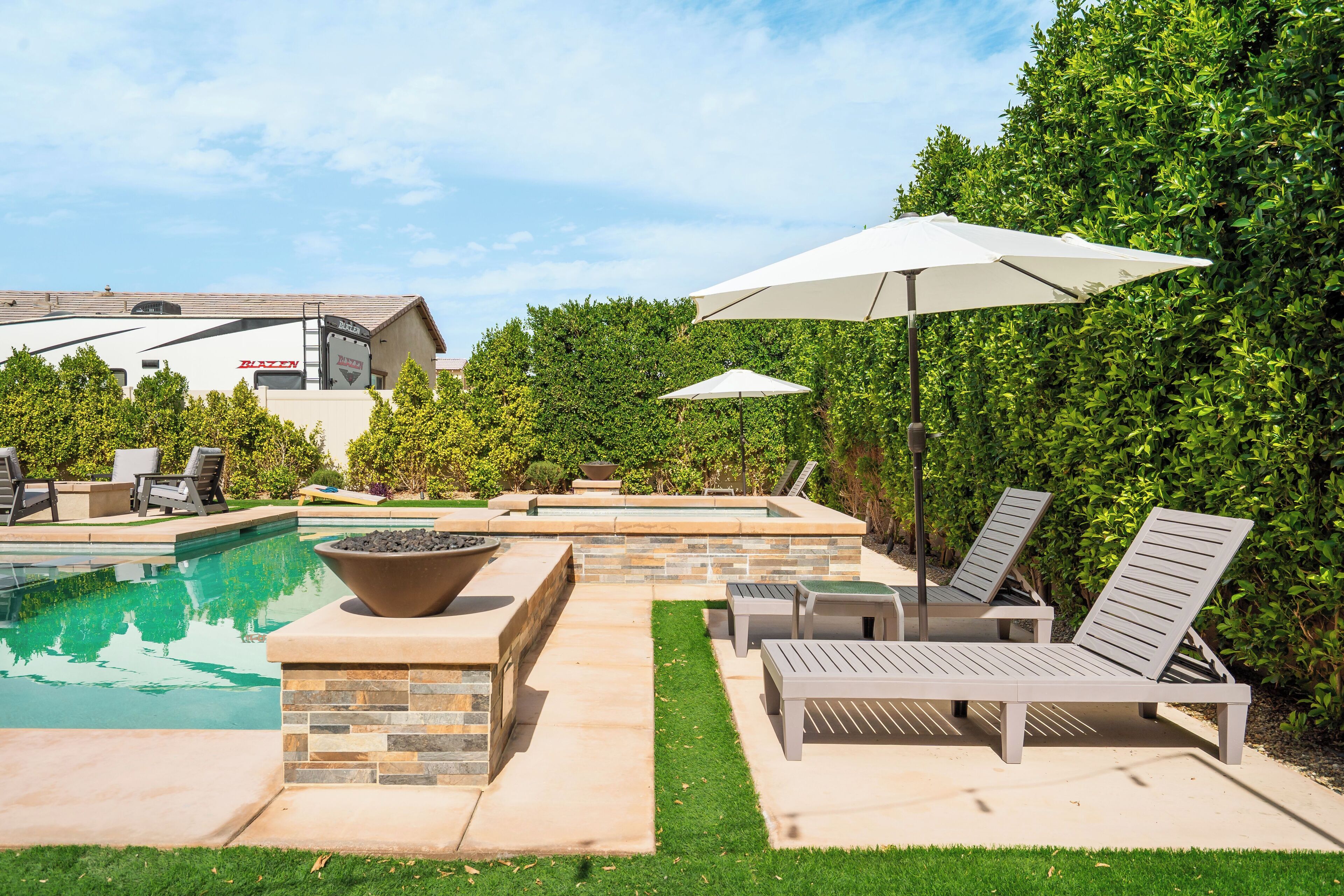 A backyard with a swimming pool, lounge chairs, and umbrellas.