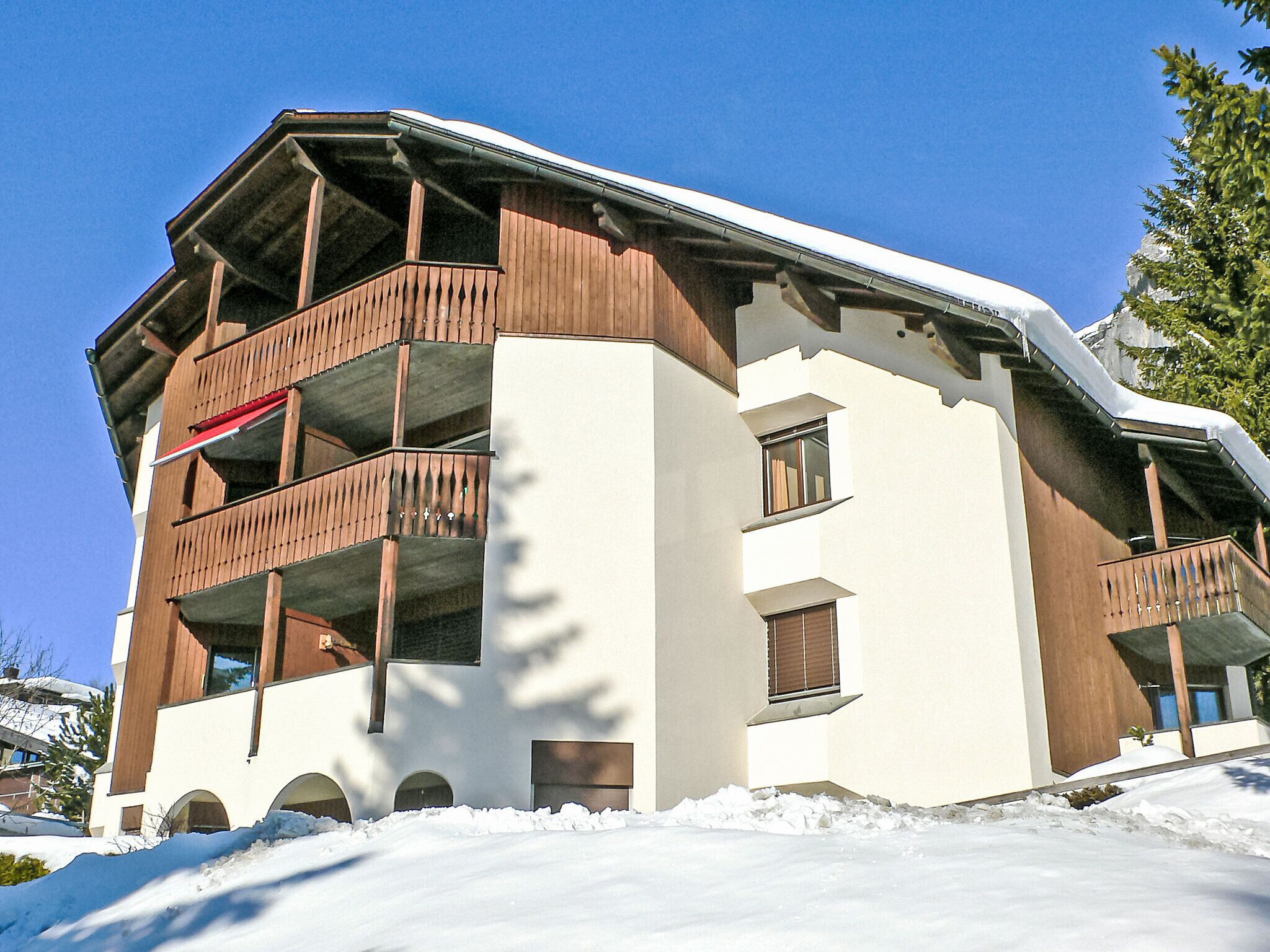 A multi-story building with balconies, large windows, and snow on the roof.