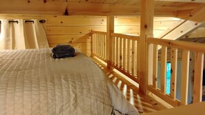 A wooden cabin room with a bed, a window, and a wooden railing. - Serenity at Nottely River (Murphy)